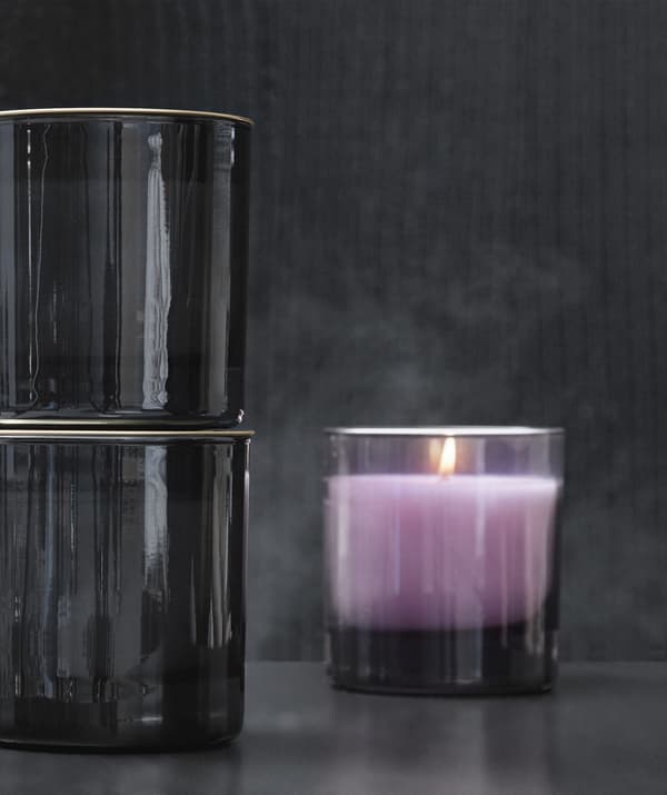 Gros plan sur une bougie couleur lavande placée dans un photophore en verre fumé