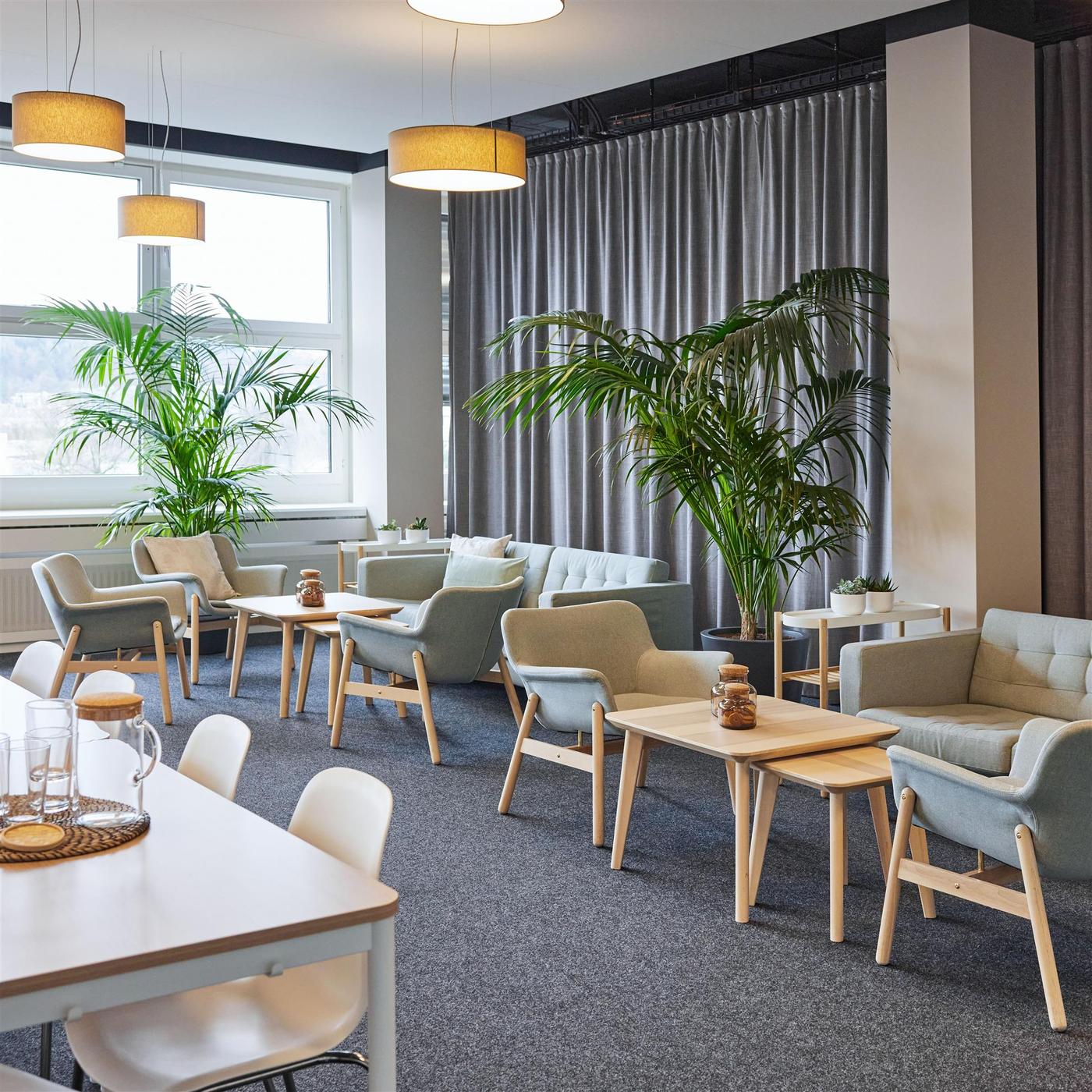 Gros plan sur une chaise de bureau de couleur naturelle avec une housse en tissu et des accoudoirs blancs, à laquelle est accroché un sac de travail beige. La chaise est placée devant un bureau blanc, près d’une fenêtre.