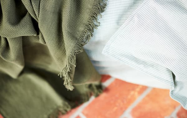 Gros-plan sur une couverture verte et un tissu rayé gris clair, posé sur un sol en pierre rouge.