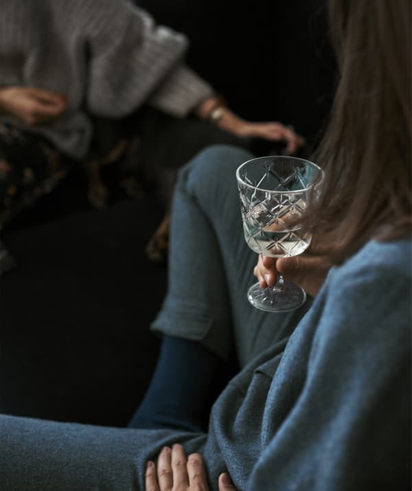 Gros plan sur une femme assise sur un canapé bleu et tenant un verre.