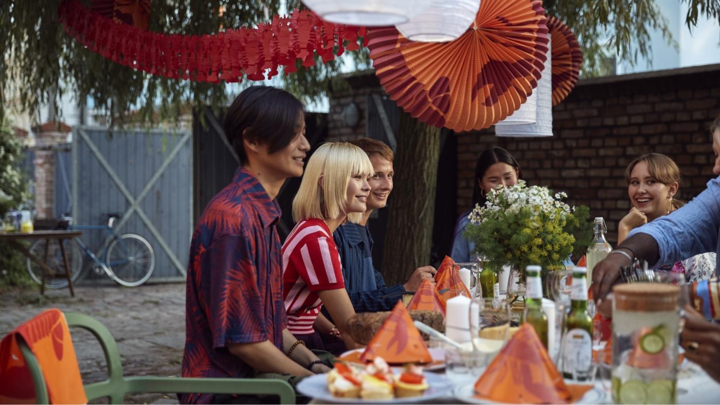 Group of friends sitting outside around a table decorated with green and red napkins, and paper decór hanging from the tree branches. 