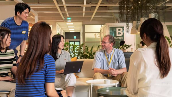 Group of IKEA co-workers meeting on sofas in a lounge area, discussing with a laptop open.