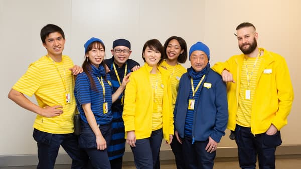 Group of IKEA coworkers in yellow and blue uniforms standing together indoors, highlighting teamwork, diversity and the IKEA workplace