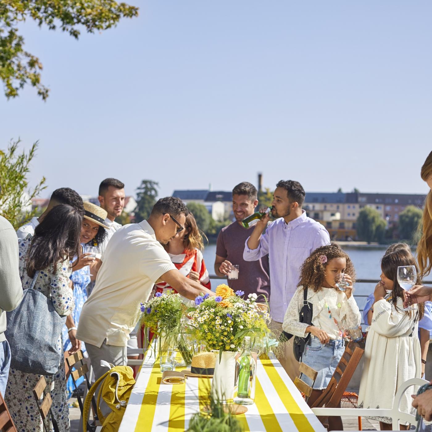 Group of people around a table decorated with white and yellow striped table cloth and fresh flowers in glass vases.