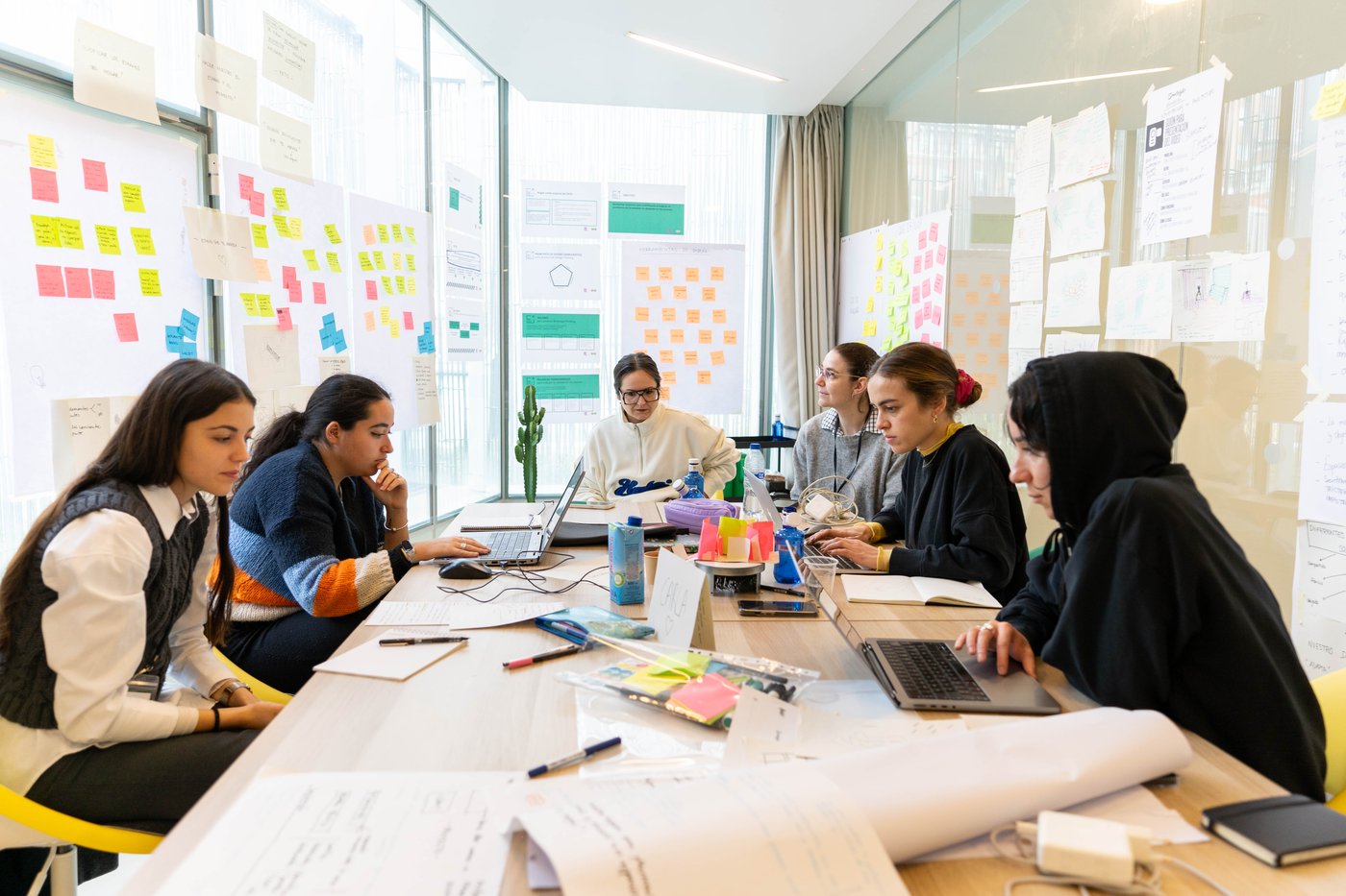 Group of six people sat at a conference table with their laptops and office supplies