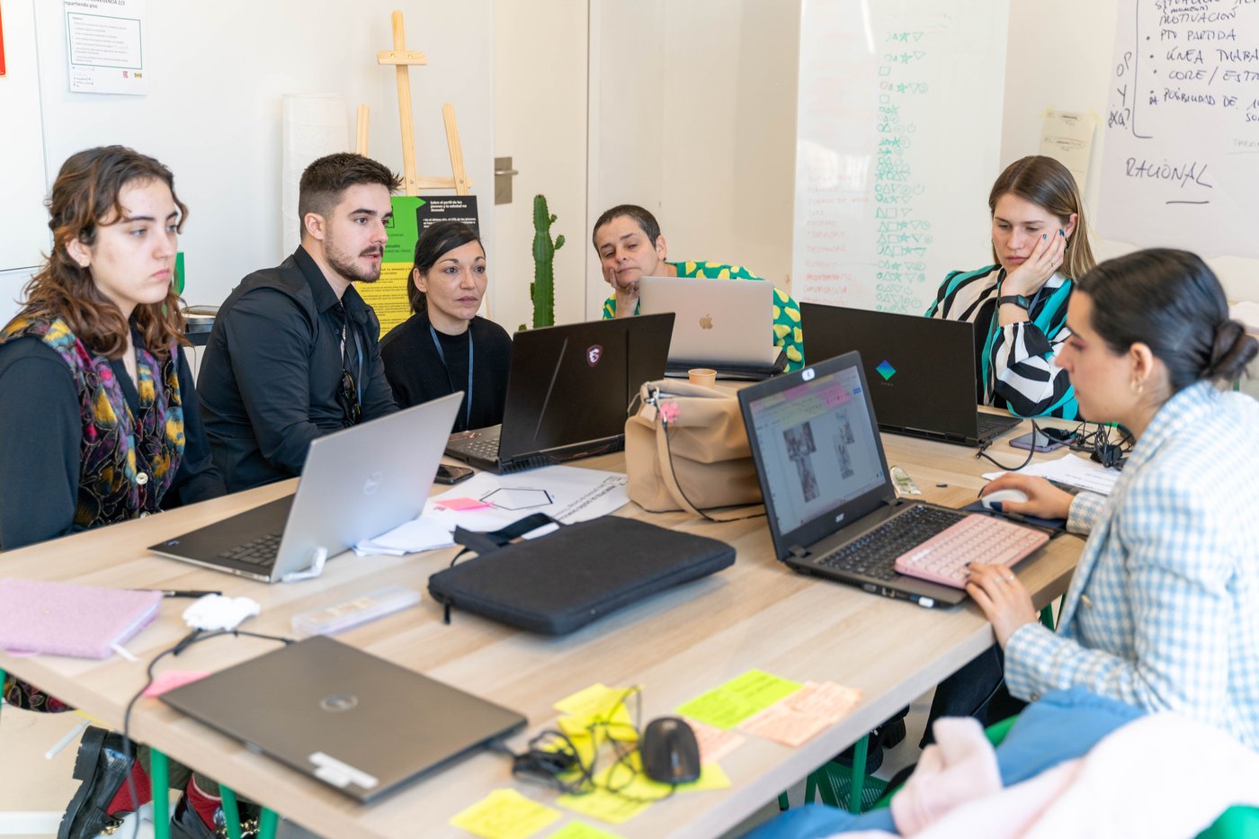 Group of six people sat at a conference table with their laptops and office supplies