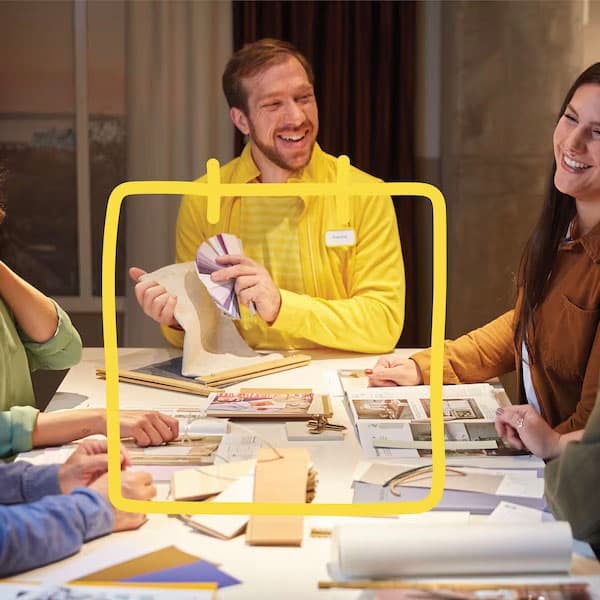 Groupe autour d'une table discute de design avec tissus, palettes de couleurs et papiers; visages flous.