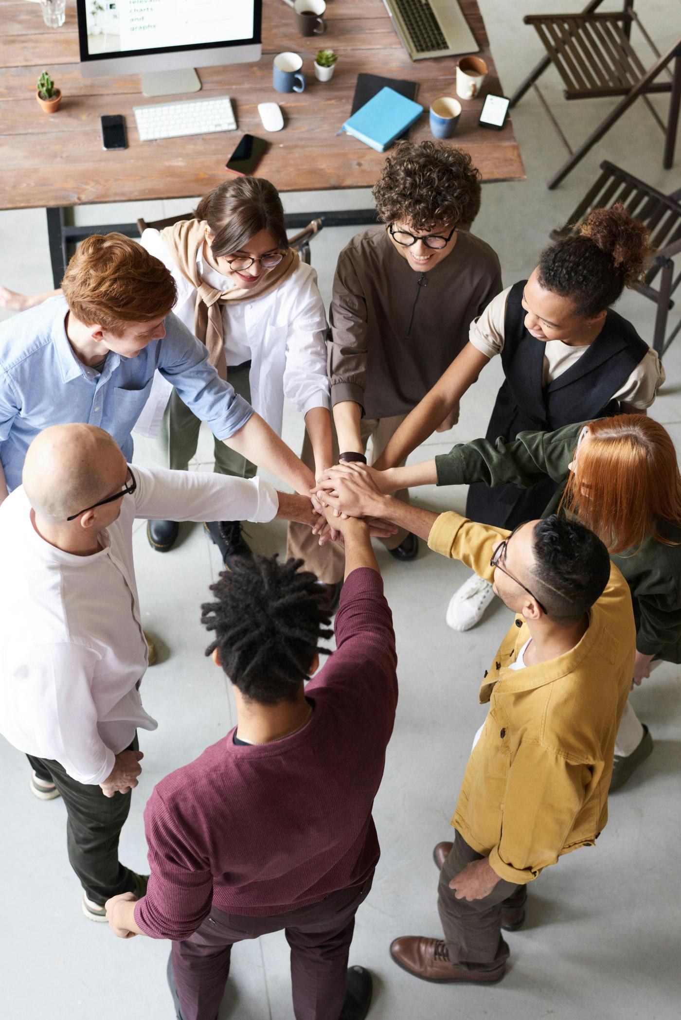 Groupe de collègues réunis autour d’un bureau, mains jointes au centre, dans un espace de travail collaboratif.
