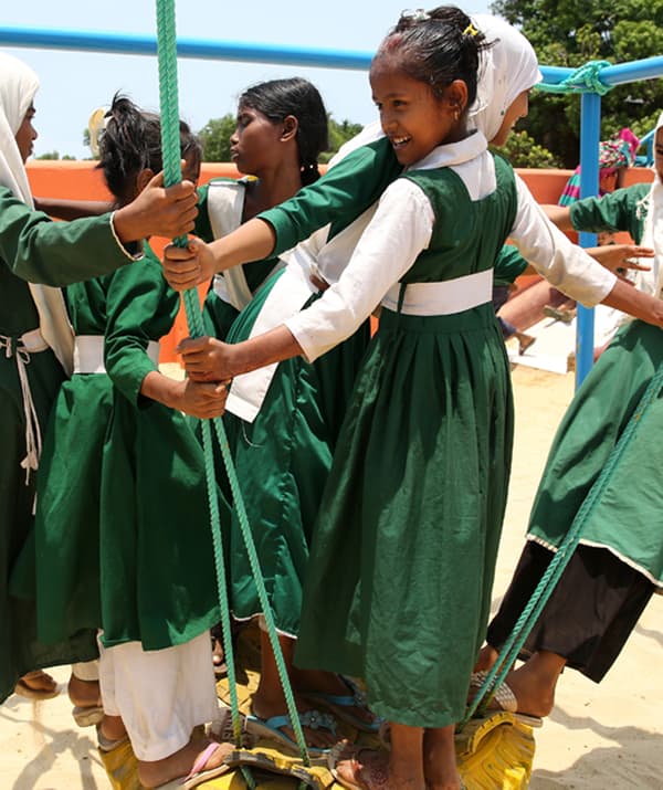 Groupe de filles en robes vertes en train de jouer dehors, sur une balançoire en cordes.