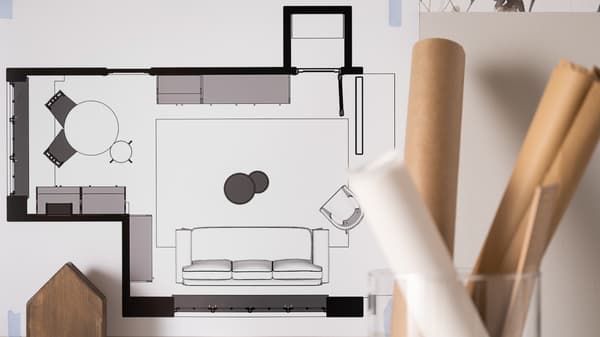 Grundriss eines Wohn- und Esszimmers. Daneben stehen Papierrollen in einer Glasvase.