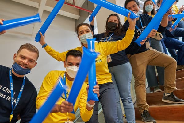 Grupo de colaboradores celebrando con globos azules y usando poleras de la empresa azules y amarillas en la escalera de la tienda.