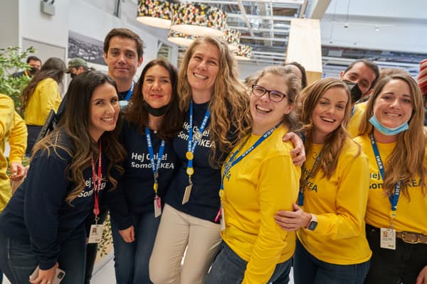Grupo de colaboradores con sus poleras azules y amarillas de manga larga riendo y sonriendo en el interior de la tienda.