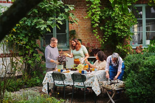 Grupo de personas en un jardín frondoso trasplantando plantas sobre una mesa con sillas alrededor.