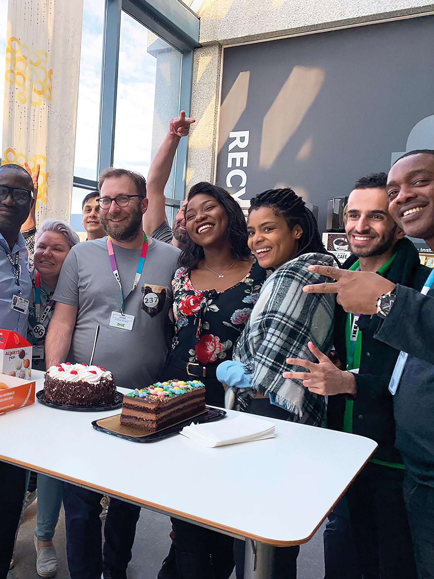 Grupo de pessoas, a sorrir lado a lado, em frente a um bolo numa festa de escritório da IKEA.
