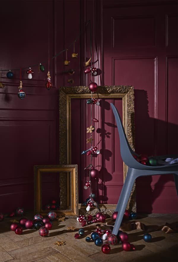 Guirlande de décorations et lumières pour le sapin de Noël, dans une pièce meublée d’une chaise et de cadres dorés.