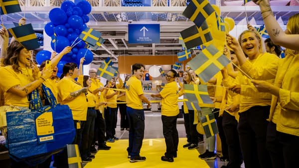 Gulklädda IKEA-medarbetare med flaggor redo att klippa bandet för att öppna.