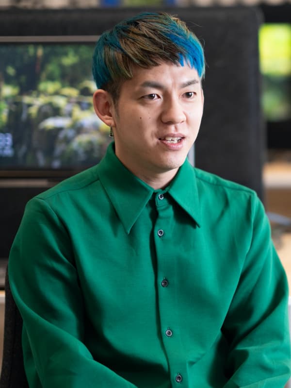 グリーンのシャツを着たコワーカーが、イケアストアの一角でインタビューに臨み、背後にディスプレイとホームファニッシングの映像が映っている。
