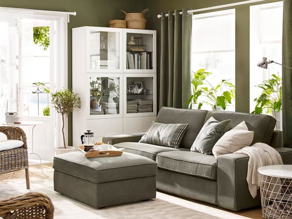 グレーのソファとオットマンを置いたナチュラルリビング。観葉植物と白いキャビネットで明るい空間。