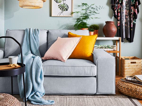 グレーソファにピンクとオレンジのクッションを合わせたリビング。ラタンの家具と柔らかな色合いが特徴。