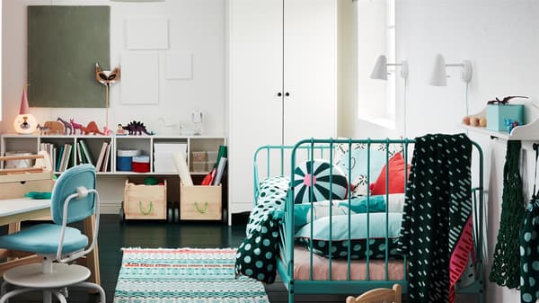 Gyerekszoba, színes szőnyegekkel, türkiz ágykerettel, fehér gardróbbal, rózsaszín függönyökkel és gyerek íróasztallal.