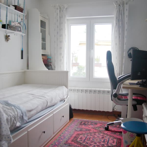Habitación de Amanda antes de la transformación, con una cama blanca y pequeña con cajones a la izquierda, una estantería blanca detrás y un escritorio gaming a la derecha. La habitación parece mucho más estrecha.