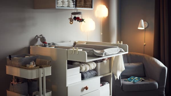 Habitación de un bebé con una cómoda blanca, un carrito y un sillón gris.