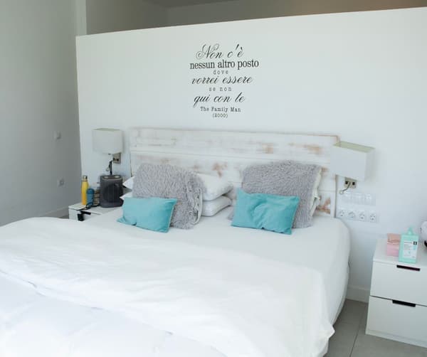 Habitación en tonos blancos, con cojines y mesillas con objetos.