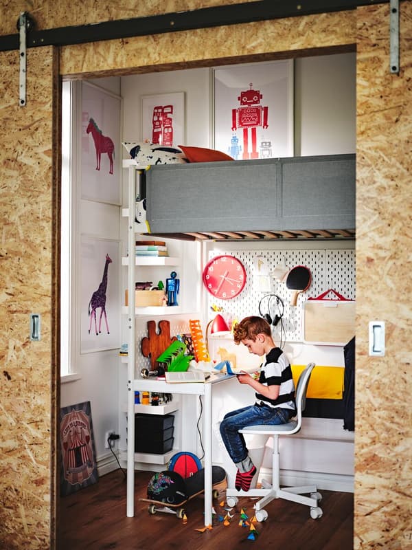 Habitación infantil con cama en litera superior y escritorio en la inferior. Niño sentado y estudiando en el escritorio.