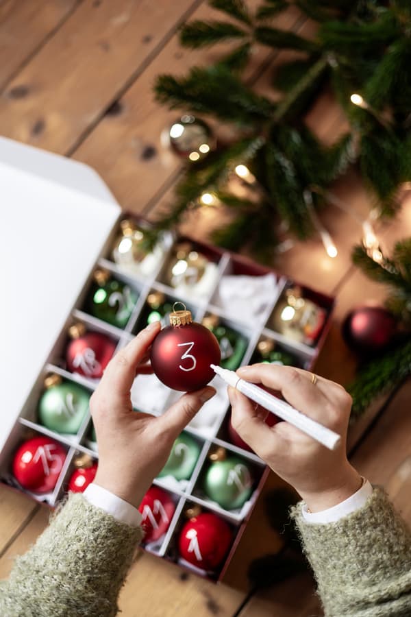 Hände beschriften eine Weihnachtskugel.