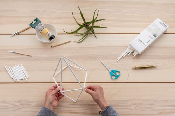 Hände binden die Strohhalme nun zu einem Diamantenmuster zusammen.