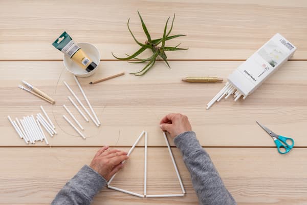 Hände binden fädeln die nächsten beiden Strohhalme auf.