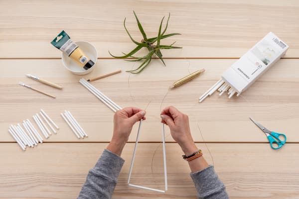 Hände fädeln die Strohhalme auf einer Schnur auf