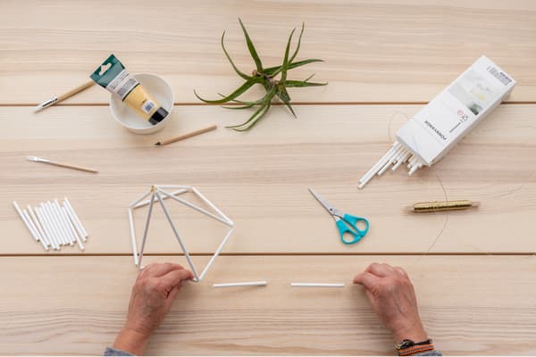 Hände fädeln weitere Strohhalme auf.