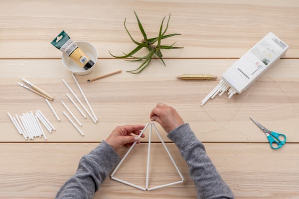 Hände verknoten die beiden Strohhalme zur Mitte hin, sodass sich ein zweites Dreieck bildet.