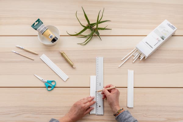 Hände zeichnen mit einem Linial die richtige Länge der Strohhalme an.