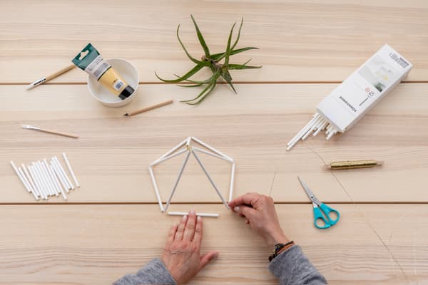 Hände zeigen, wie die Strohhalme aufgefädelt werden müssen, damit eine Pyramide entsteht.