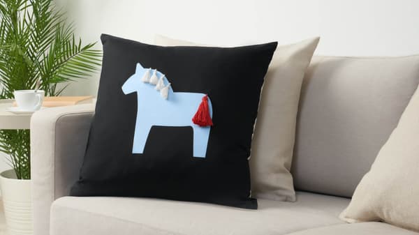 HÄSTHAGE cushion and throw on a sofa in a dimly lit room.