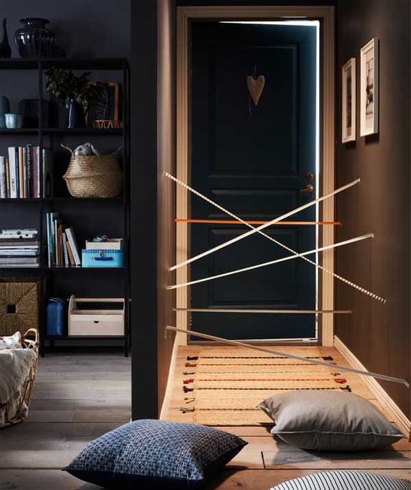 Hall de entrada, ao lado da sala, com fita adesiva em ziguezague a imitar raios laser. Tapete e almofadas espalhados no chão.