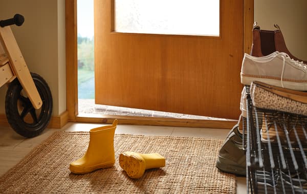 Hall d’entrée avec une paire de bottes d’enfant sur le tapis, une étagère à chaussures sur le côté, un vélo d’enfant en bois contre le mur.