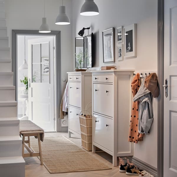 Hall d’entrée blanc avec deux armoires à chaussures HEMNES blanches de style traditionnel placées côté à côte et une rangée de crochets pour les manteaux.