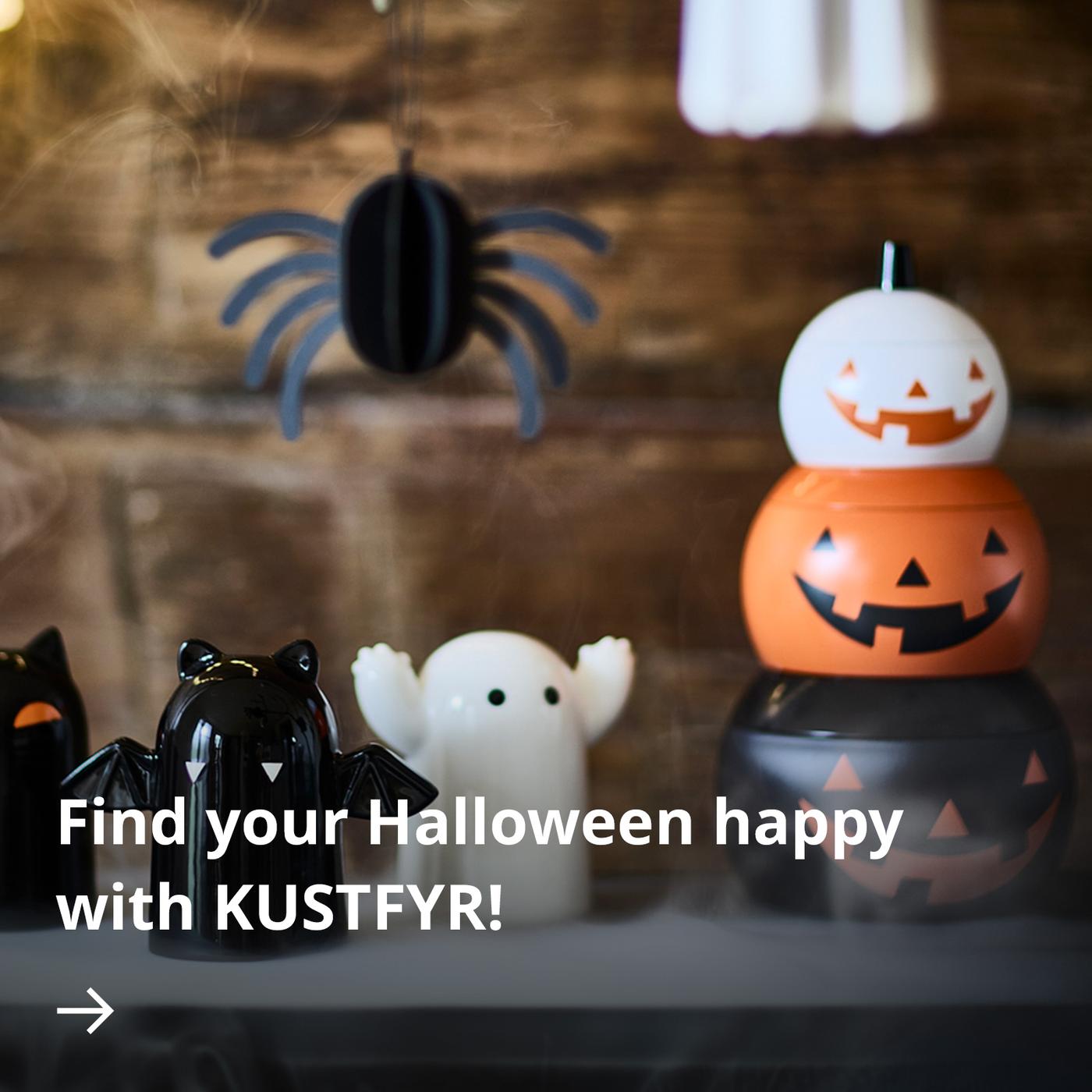 Halloween-themed decorations, including three cat-, ghost- and bat-shaped figures, a hanging spider decoration, white ghosts and stacked pumpkin-shaped tins, displayed on a table.