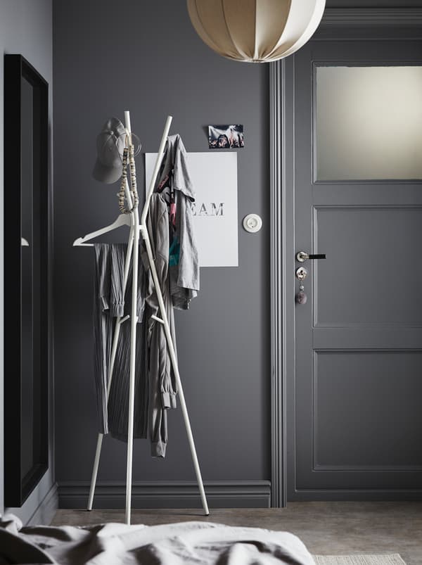 Hallway area in a grey colour scheme. By the front door stands an EKRAR hat and coat stand, holding various garments.