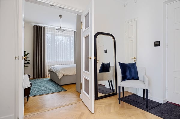 Hallway view into bedroom with floor-length mirror and modern chair