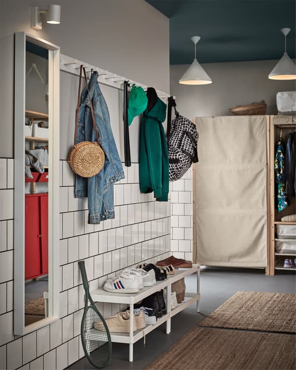 Hallway with white mirror, white pendant lamps, white wall lamp, white racks with knobs, white shoe racks and two jute rugs.
