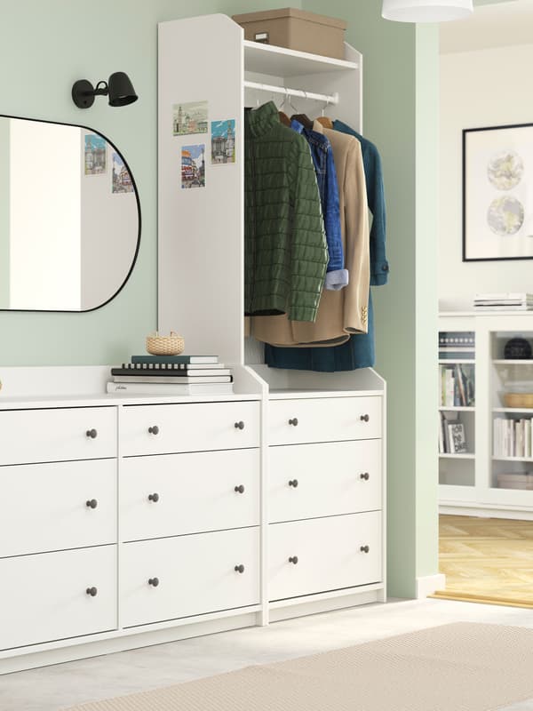 Hallway with wide, white HAUGA chest and wardrobe combo. In the adjacent living room stands a white HAUGA glass-door cabinet.