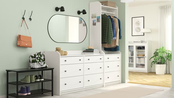 Hallway with wide, white HAUGA chest and wardrobe combo. In the adjacent living room stands a white HAUGA glass-door cabinet.