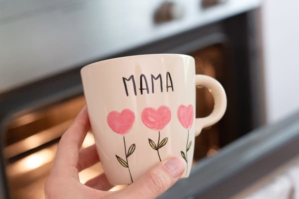 Hand hält die bemalte Tasse vor einem Backofen.