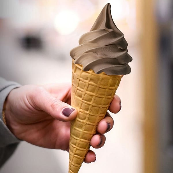Hand holding a cone with a tall swirl of soft chocolate ice cream.
