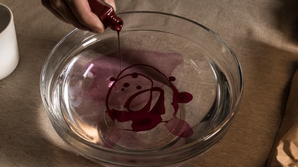 Hand som droppar och häller rött nagellack i en djup skål med vatten. 