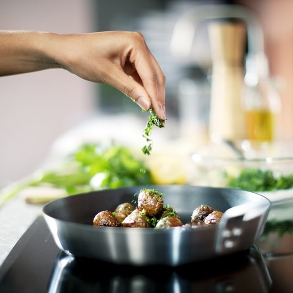 Hand sprinkling fresh herbs into a pan of meatballs cooking on the hob.